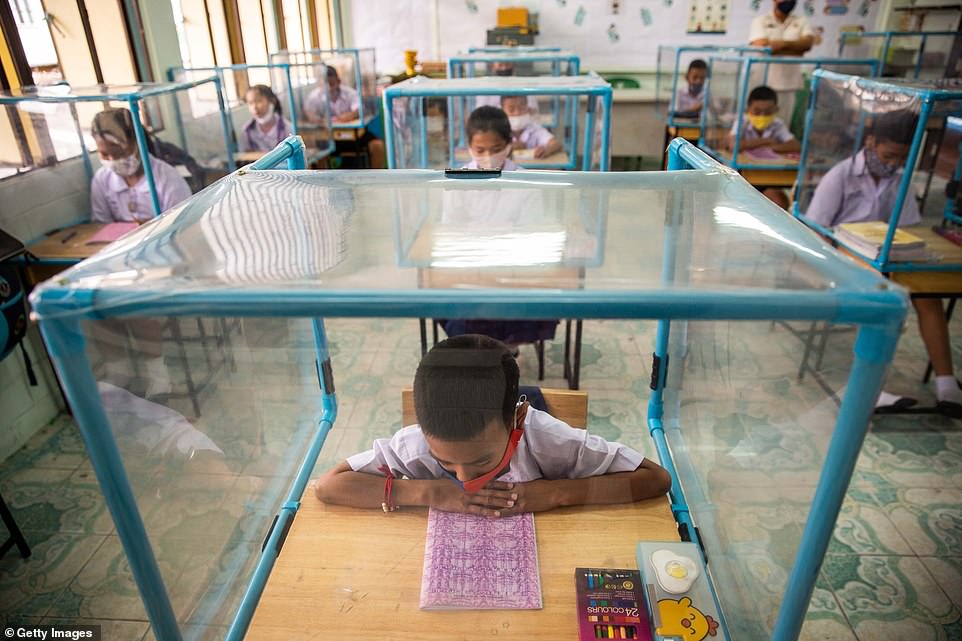 A Thai student prepares for his lesson at school while at a desk with a protective screen